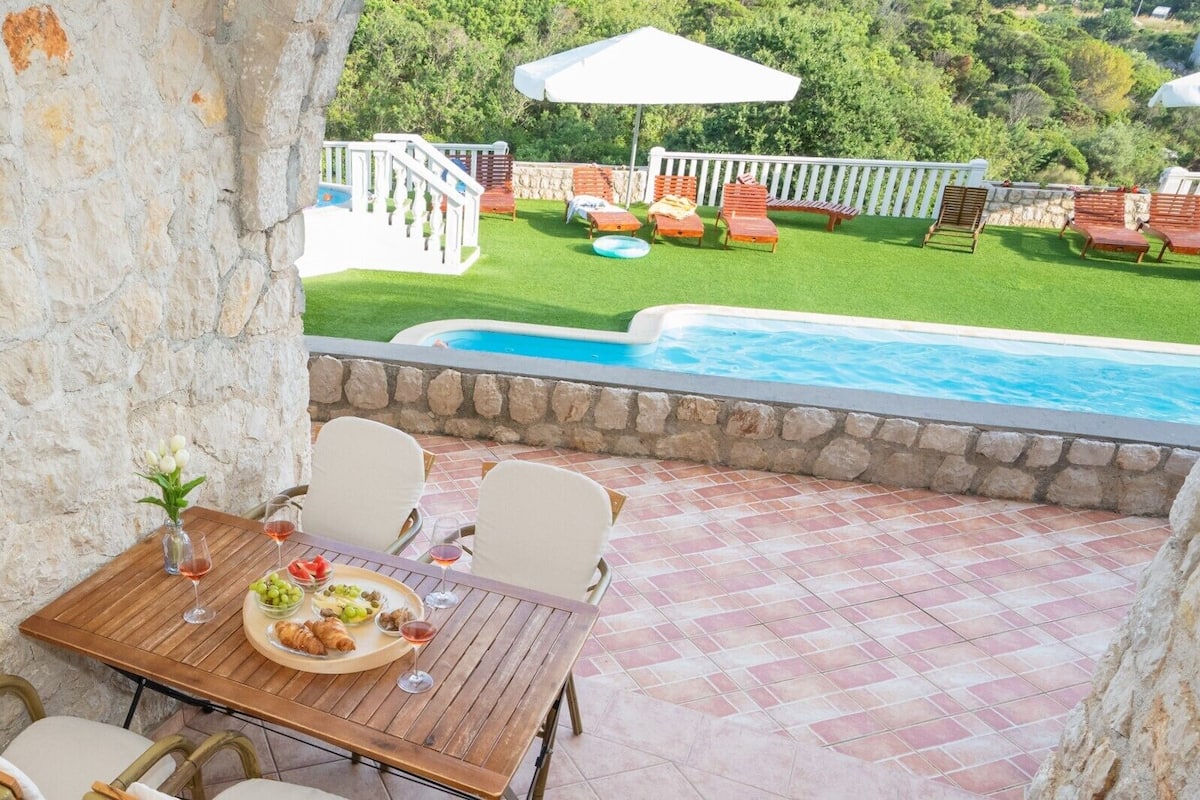 Une terrasse avec une table dressée pour deux personnes, une piscine et, au fond, une clôture blanche.