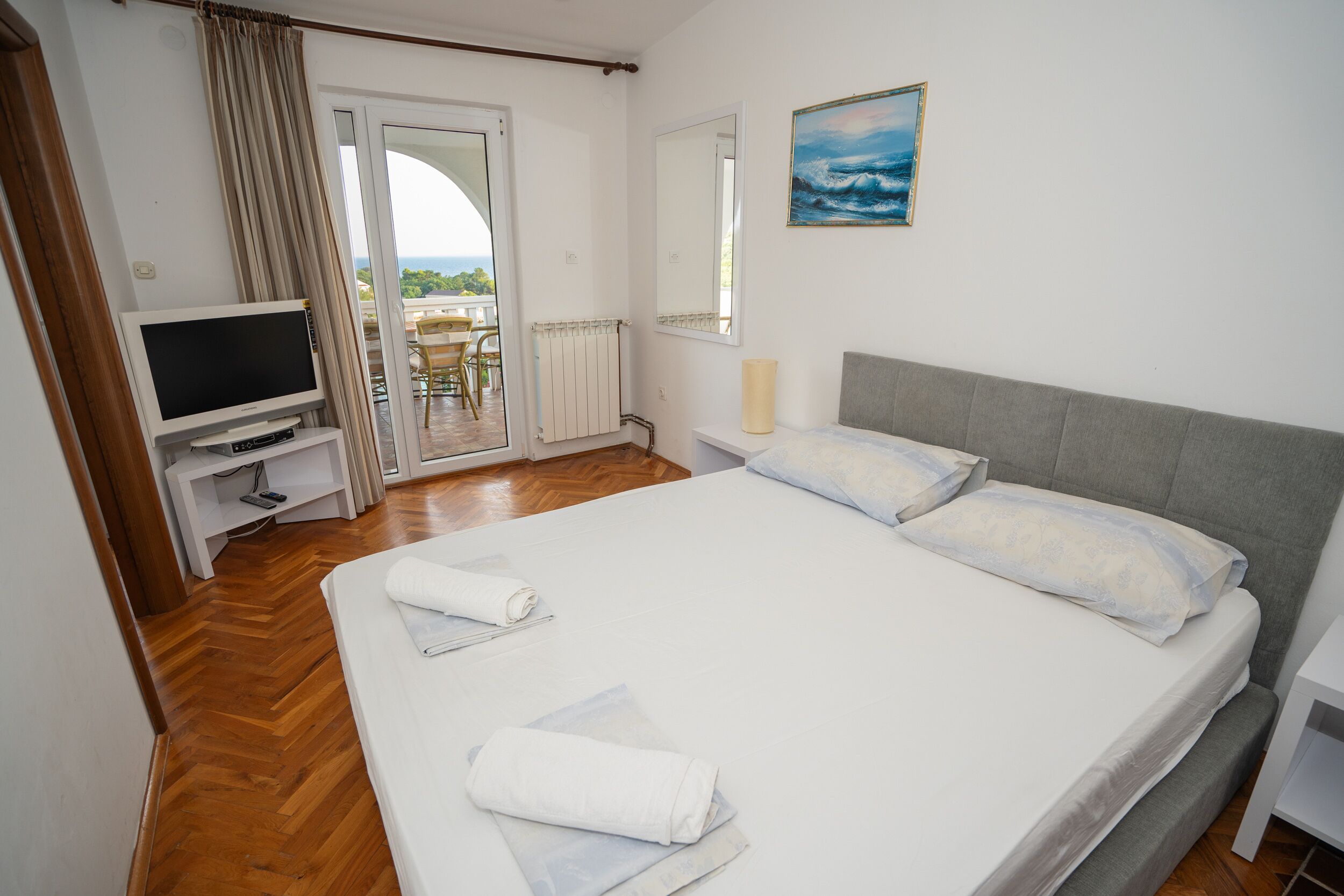 A bedroom with a bed, a TV, a painting, and a view through a door.