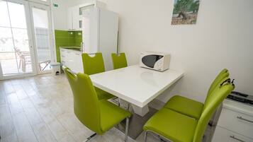 Un comedor con una mesa blanca, sillas verdes, un microondas y un cuadro en la pared.