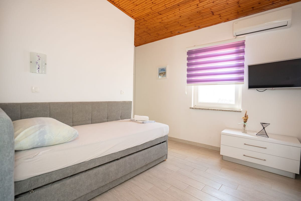 Une chambre à coucher avec un lit, une table de chevet, une télévision et une fenêtre avec des stores.