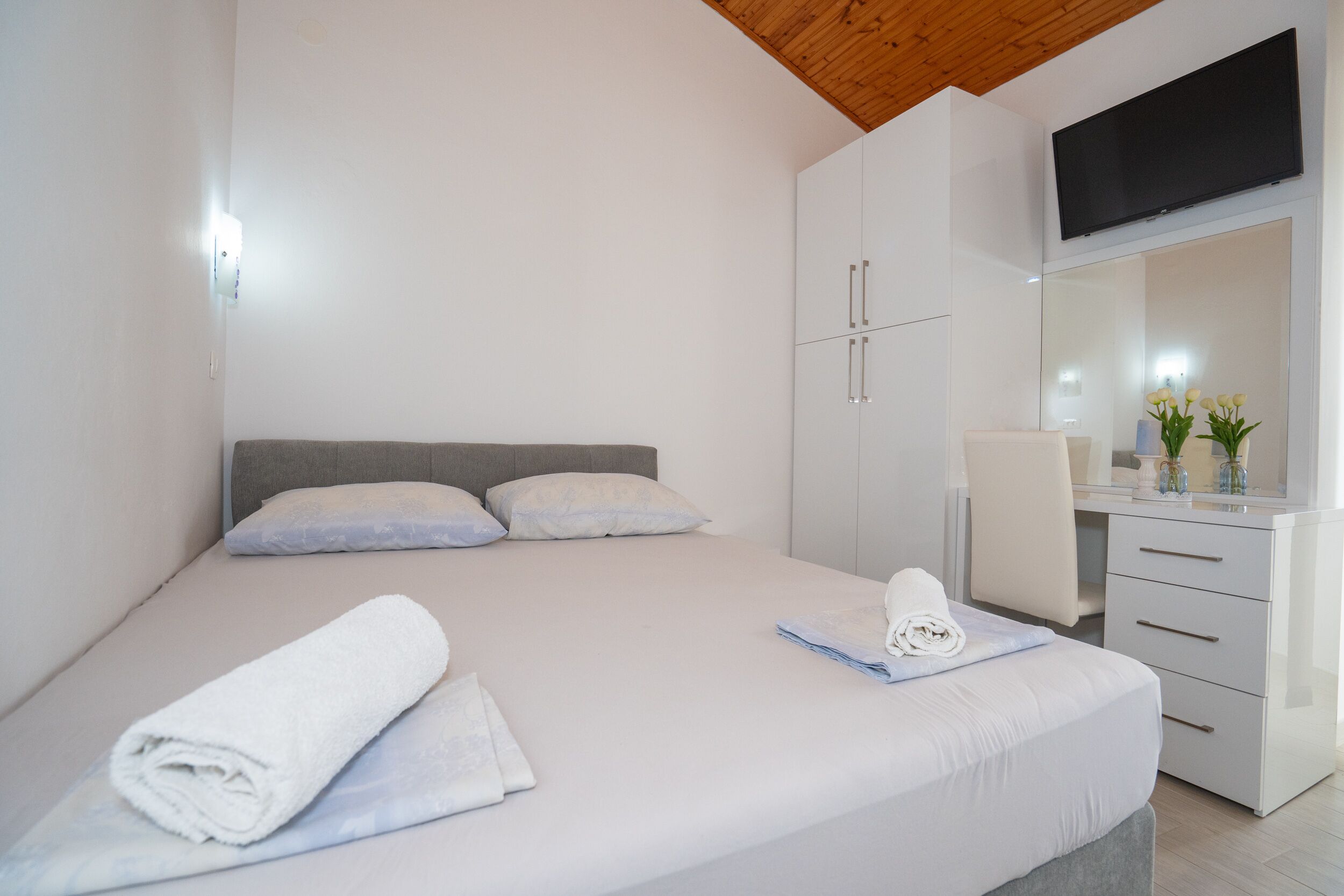 Un dormitorio moderno con cama, escritorio, silla y televisor montado en la pared.