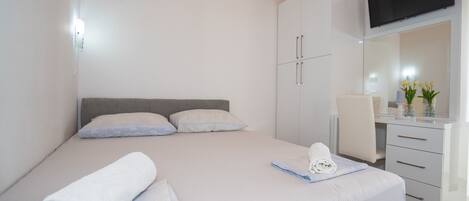 A modern bedroom with a bed, a desk, a chair, and a TV mounted on the wall.