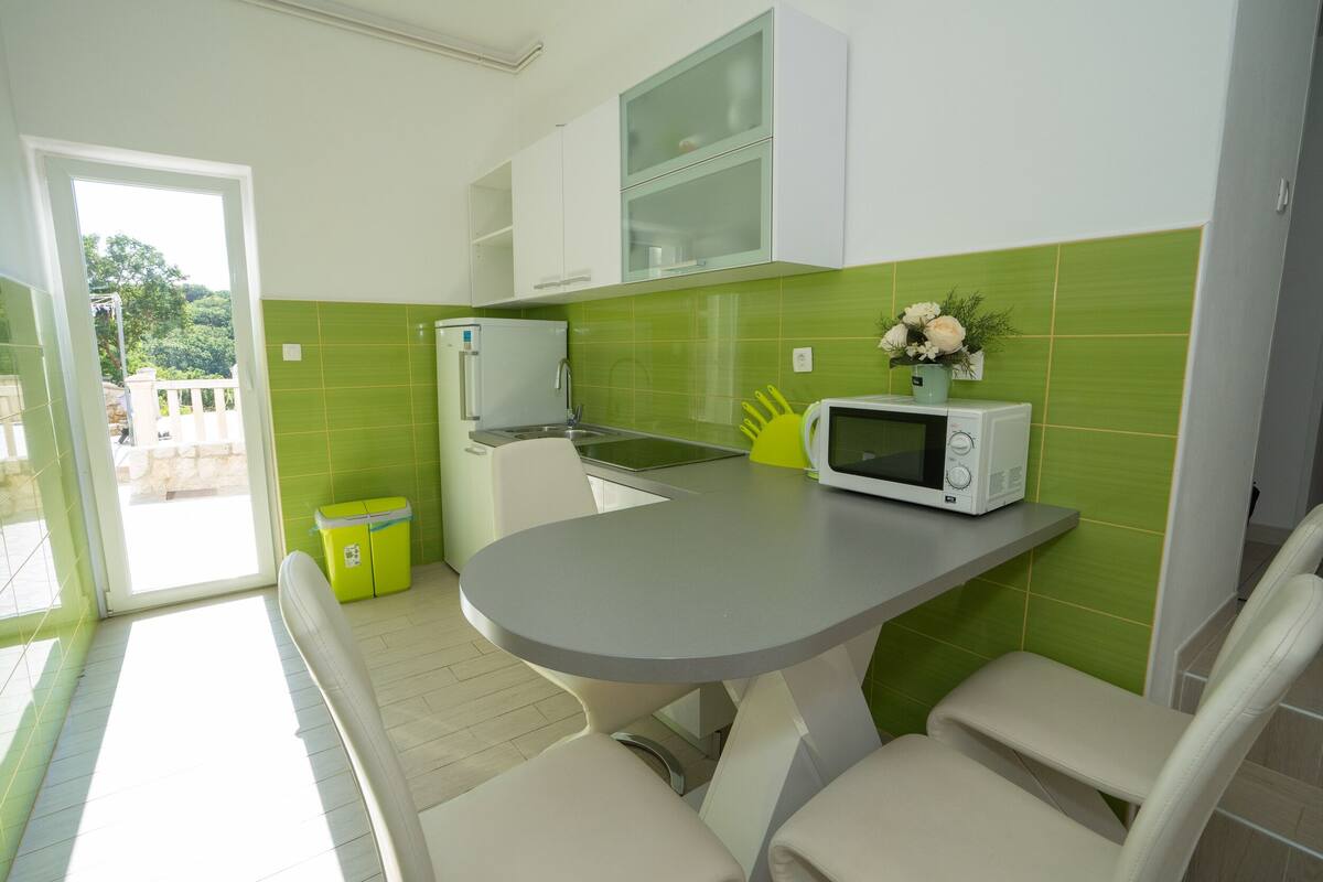 Une cuisine compacte avec un coin repas, comprenant un four à micro-ondes, un petit évier et un plan de travail recouvert de carreaux verts.