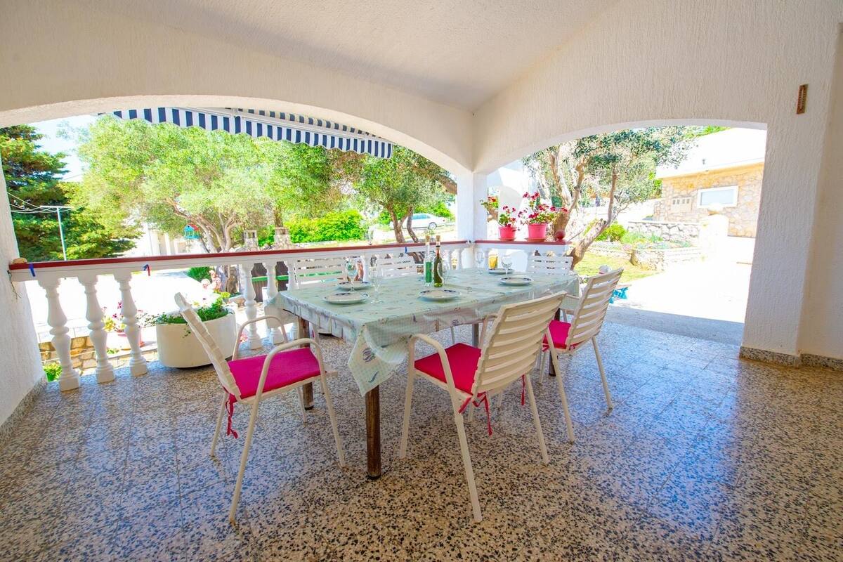 Une terrasse extérieure avec une table ronde, des chaises blanches dotées de coussins rouges et une balustrade blanche.