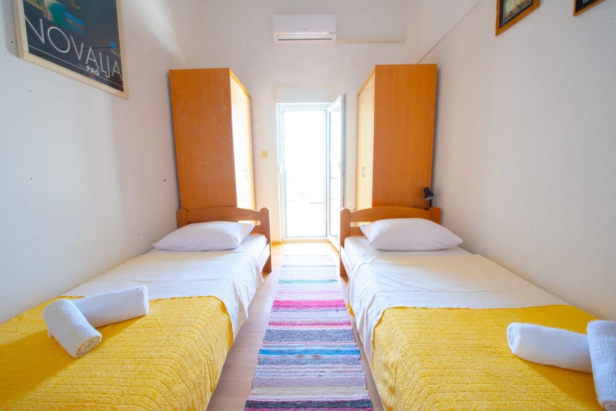 Une chambre avec deux lits, un tapis rayé aux couleurs vives et une grande fenêtre.