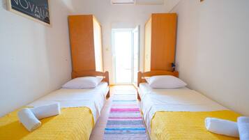 A room with two beds, a colorful striped rug, and a bright window.