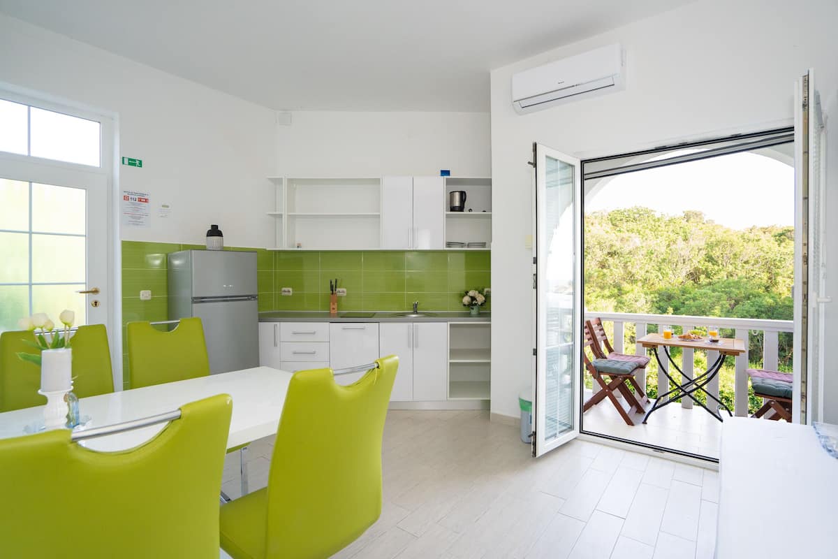 Une cuisine lumineuse avec des meubles blancs, un pare-feu vert et un coin repas comprenant une table blanche et des chaises vertes.