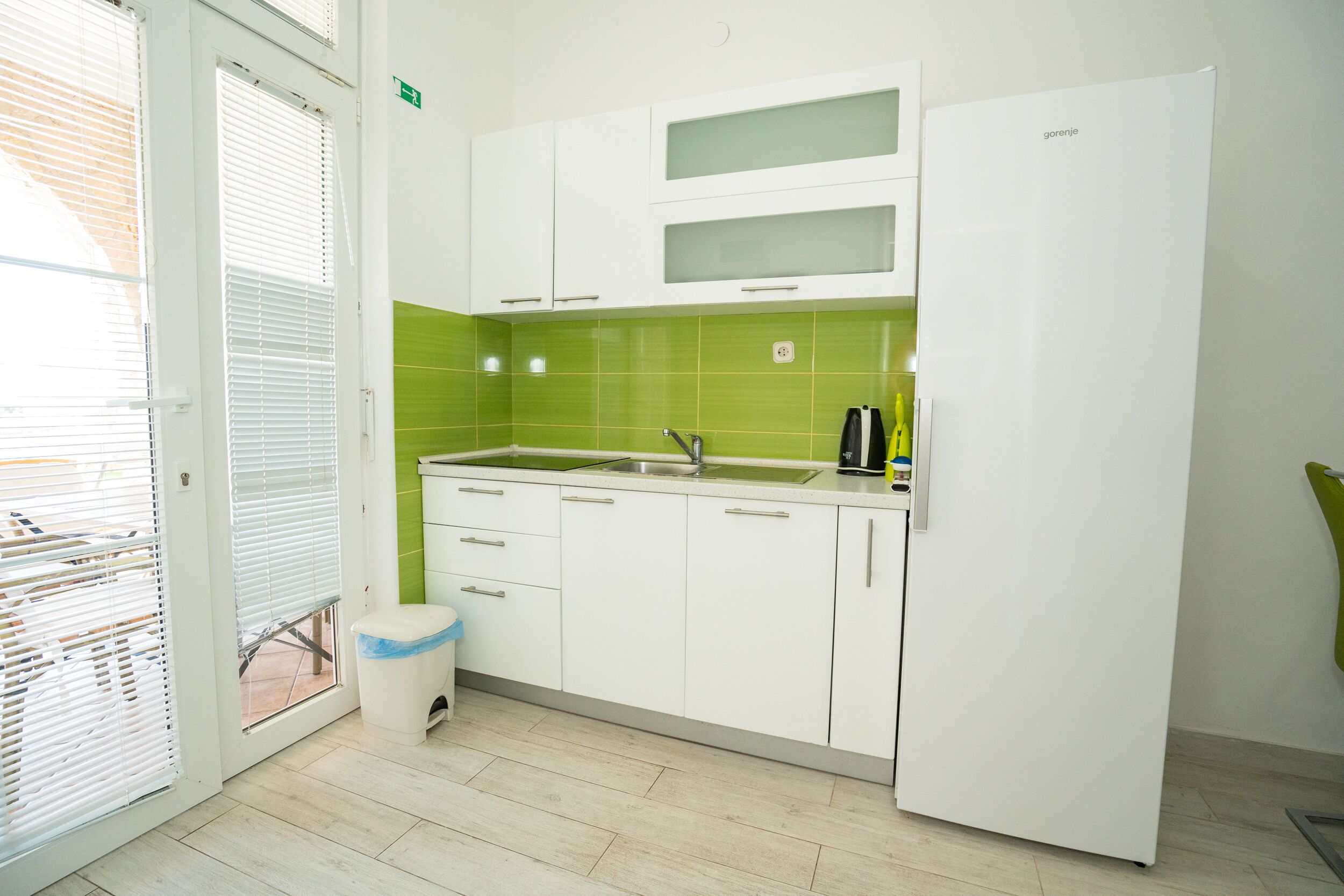 A modern kitchen with white cabinets, a green backsplash, and a built-in refrigerator.