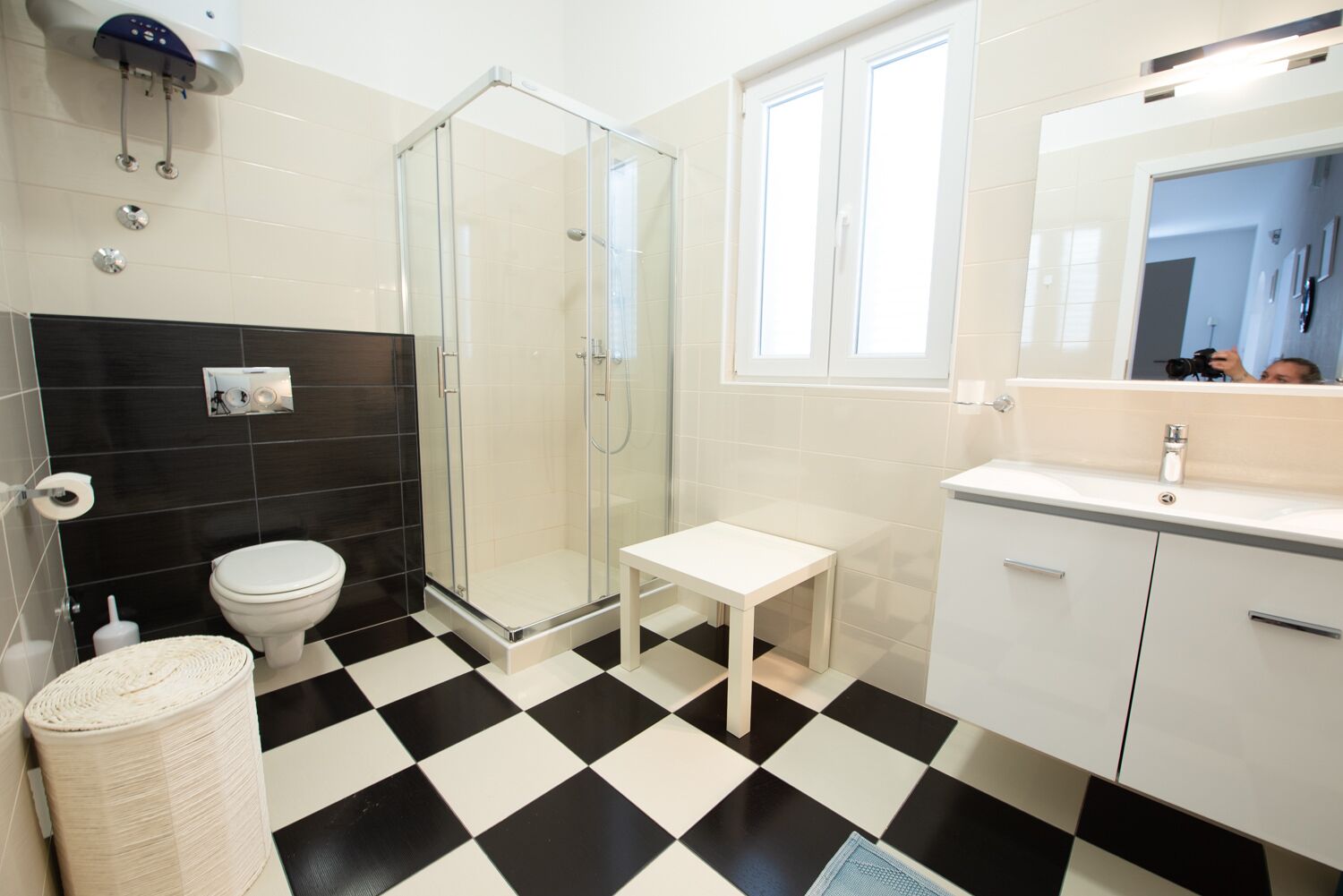 A bathroom with a glass-enclosed shower, a toilet, a small white table, and a sink with a mirror.