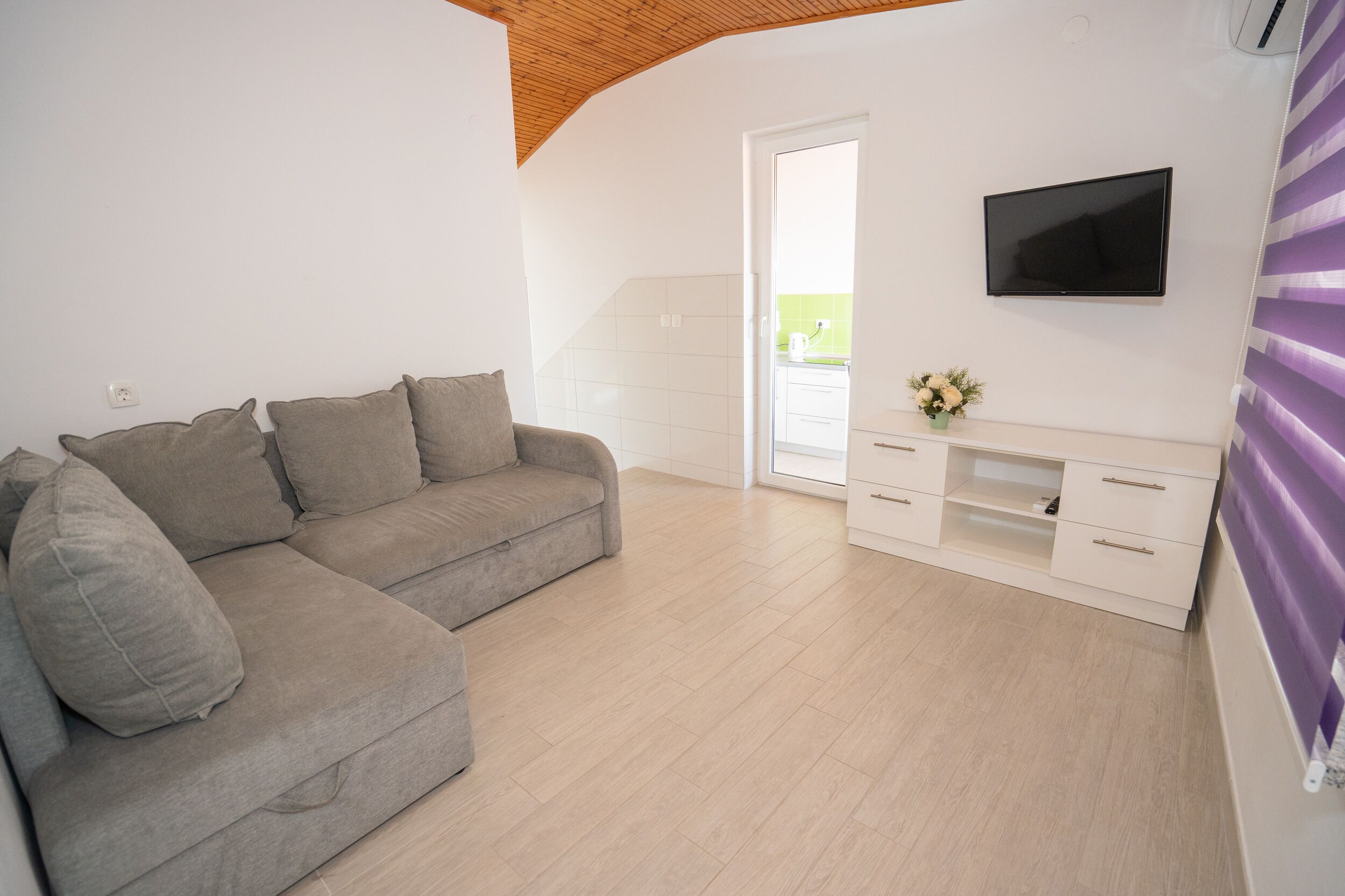 Ein modernes Wohnzimmer mit einem grauen Sofa, einem Flachbildfernseher und einem weißen Schrank.