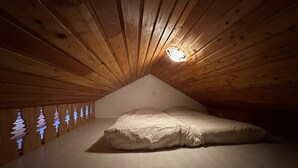 Une chambre avec un plafond en pente, des murs en bois, un lit avec une literie blanche et un luminaire fixé au mur.