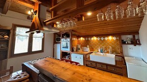 Une cuisine rustique avec des poutres en bois, une table en bois, un évier et des verres suspendus.