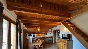 Une cuisine rustique avec des poutres en bois, une cheminée en pierre et un coin repas comprenant une table et des chaises en bois.