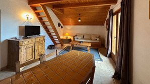 Une pièce chaleureuse avec un plafond en bois, un canapé, une table et un téléviseur posé sur un meuble.