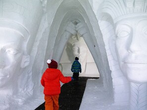 Een persoon in een rode jas en een ander in een blauwe jas lopen door een tunnel met een groot standbeeld.