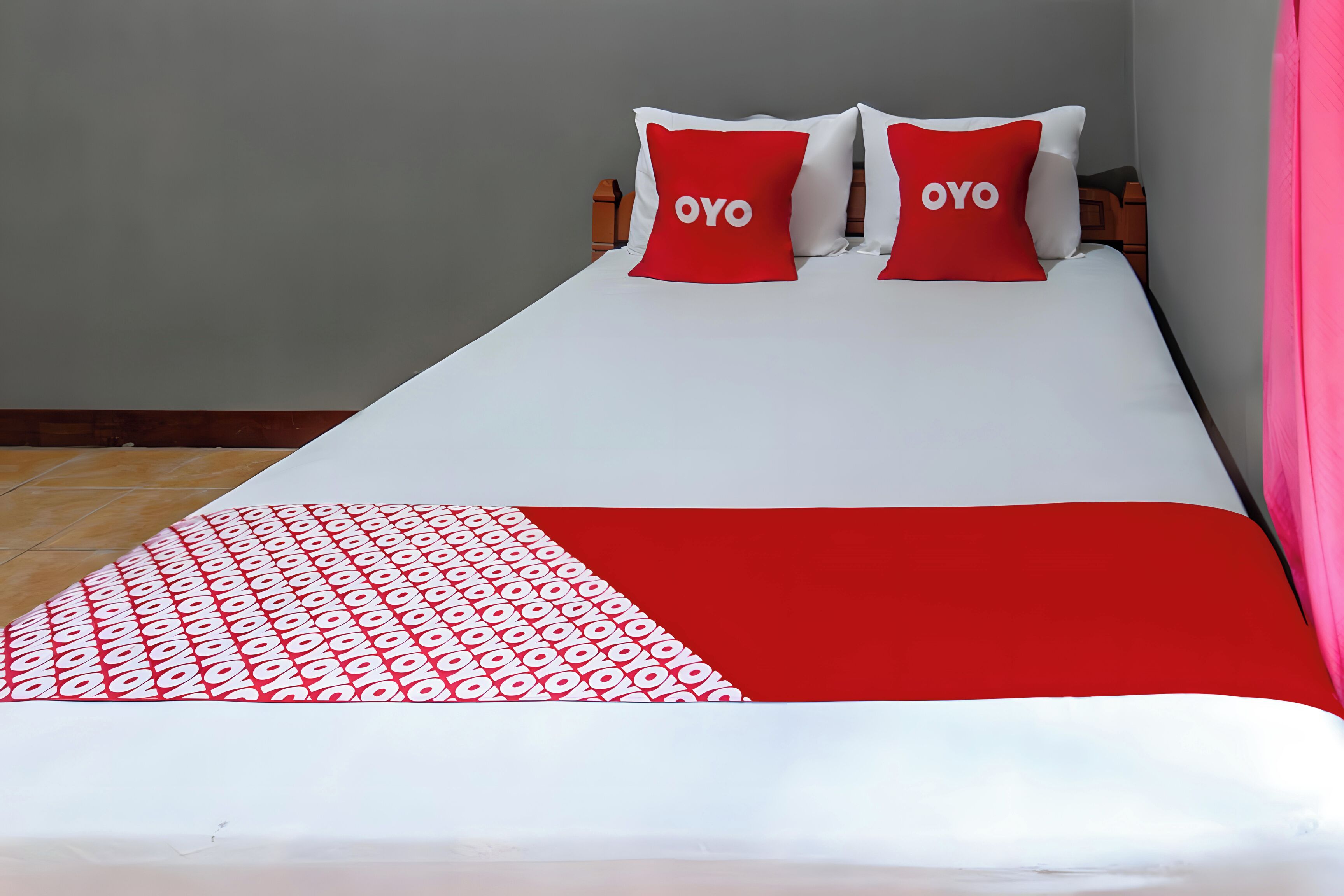 Una cama con una colcha blanca y roja, dos almohadas con la palabra 'OYO' y una manta estampada.