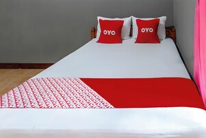 Una cama con una colcha blanca y roja, dos almohadas con la palabra 'OYO' y una manta estampada.