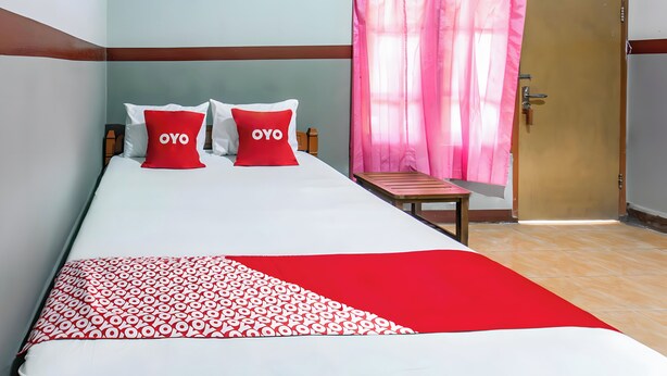 Ein Bett mit zwei Kissen, eine Bank und eine Tür mit einem rosa Vorhang.