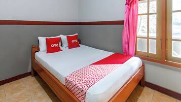 Una cama con una colcha blanca y roja estampada, dos almohadas con la palabra 'OYO' y una cortina rosa en una ventana.