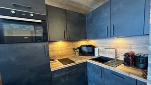 A modern kitchen with dark cabinets, a wooden countertop, a built-in oven, a microwave, a sink, and a toaster.