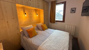A bedroom with a wooden headboard, two bedside lamps, a window with curtains, and a radiator.