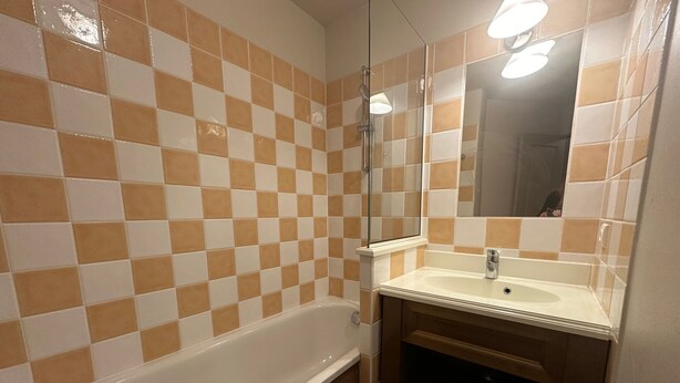 A bathroom with a checkered tile wall, a white bathtub, a sink with a mirror, and wooden cabinets. - Bright ski-in/ski-out apartment with balcony in Vars Les Claux (Vars)