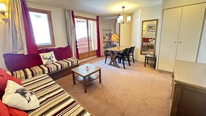 A living room with a sofa, coffee table, and dining table. There is a kitchen area with cabinets and a window. - Bright ski-in/ski-out apartment with balcony in Vars Les Claux (Vars)