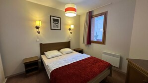 A bedroom with a bed, bedside tables, a window with curtains, a radiator, and wall-mounted lights. - Bright ski-in/ski-out apartment with balcony in Vars Les Claux (Vars)