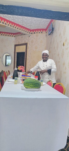 A person standing by a table with food items and a watermelon centerpiece. - KIVULI VILLAS (Diani Beach)