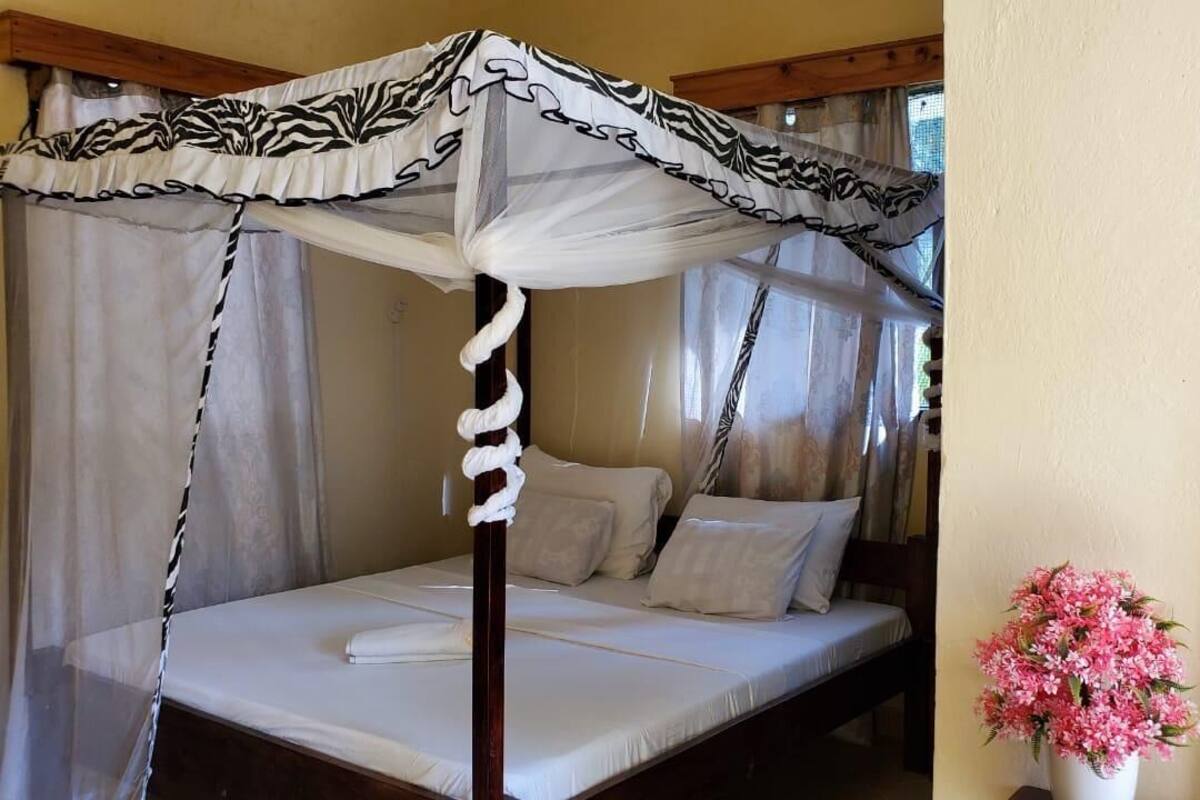 A four-poster canopy bed with white linens and a floral vase on the nightstand.