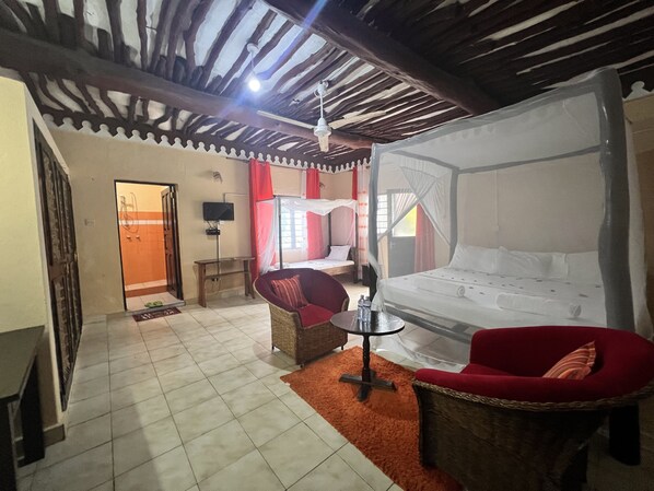 A room with a bed, two chairs, a small table, a TV, and a ceiling fan. - KIVULI VILLAS (Diani Beach)