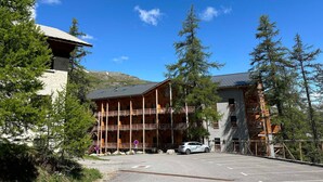 Un chalet à plusieurs étages doté de balcons, d’un espace de stationnement et surplombant un paysage montagneux.