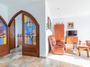 A living room with a brown leather sofa, wooden cabinet, and a television. - Spacious Villa with Pool, Garden, BBQ, A/C, WiFi, Parking - Walk to Beach (Sant Pere Pescador)