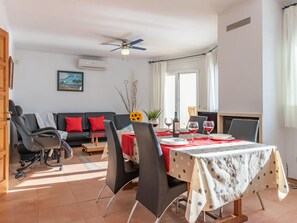 A dining area with a table set for four, a ceiling fan, a sofa with red cushions, and a painting on the wall.
