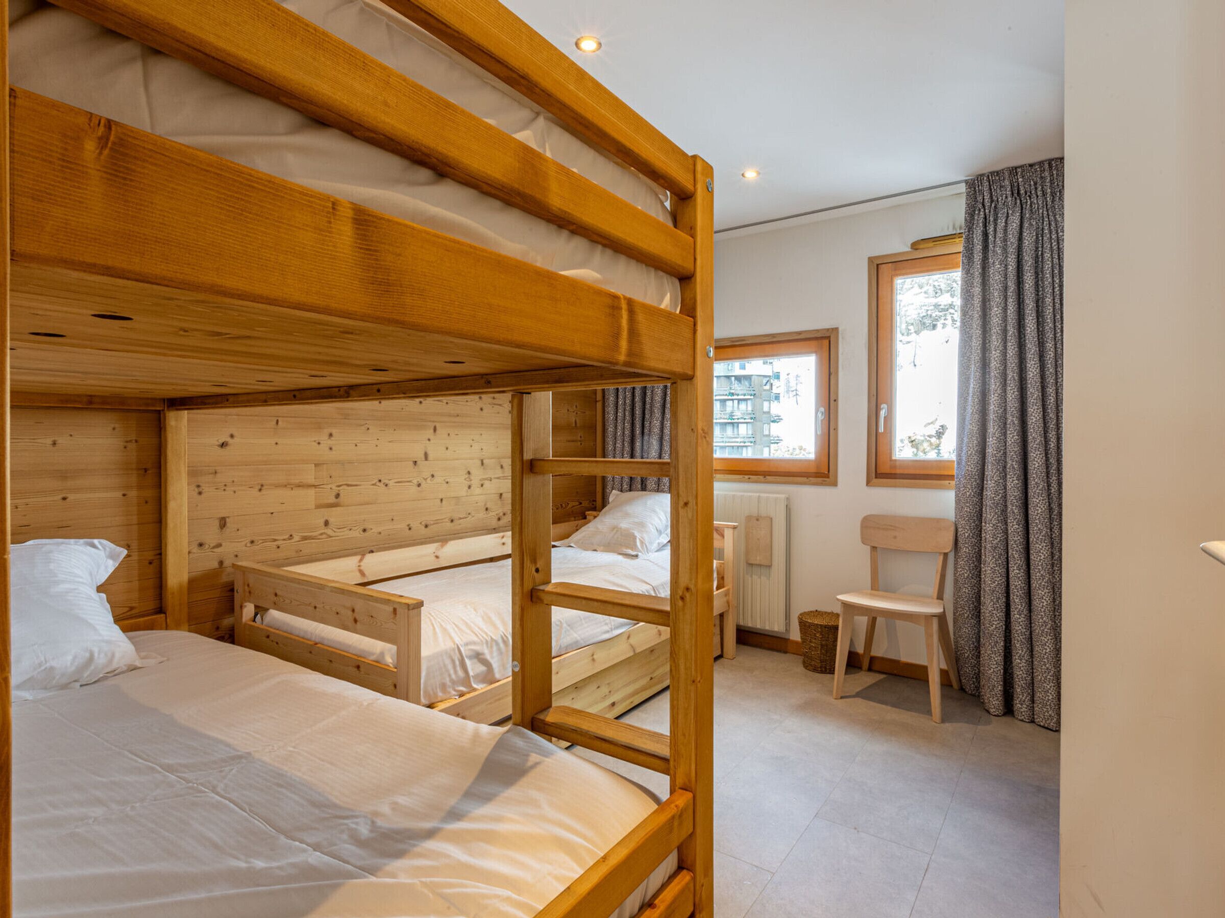 A bunk bed room with wooden walls, a window, and a chair.