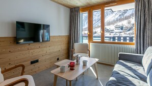 A cozy room with a wooden ceiling, a flat-screen TV mounted on the wall, a wooden table with two cups, a chair, and a sofa. - Val d'Isère: Renovated 1-Bed Apartment, Ski-In/Ski-Out, Sleeps 4, Stunning Mountain Views (Val-d'Isère)