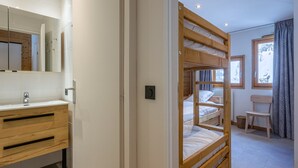 A bedroom with a bunk bed, a wooden dresser, a mirror, and a window with a view of trees. - Val d'Isère: Renovated 1-Bed Apartment, Ski-In/Ski-Out, Sleeps 4, Stunning Mountain Views (Val-d'Isère)