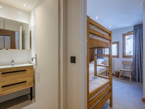 Quarto com beliche, cómoda de madeira, espelho e janela com vista para árvores.