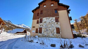 A multi-story building with a stone facade and wooden upper levels, set against a snowy mountain backdrop. - Spacious T3 near slopes, south terrace, with WIFI, for 6 people (Vars)