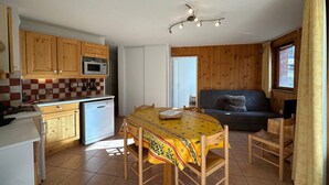 A compact kitchen with wooden cabinets, a microwave, and a dishwasher. There's a dining table with chairs and a sofa in a cozy corner. - Spacious T3 near slopes, south terrace, with WIFI, for 6 people (Vars)