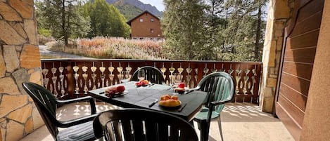 An outdoor dining area with a table set for four, surrounded by stone walls and a view of a mountain.