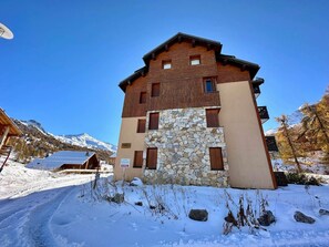 A two-story building with a stone facade and wooden upper levels, set against a snowy mountain backdrop.