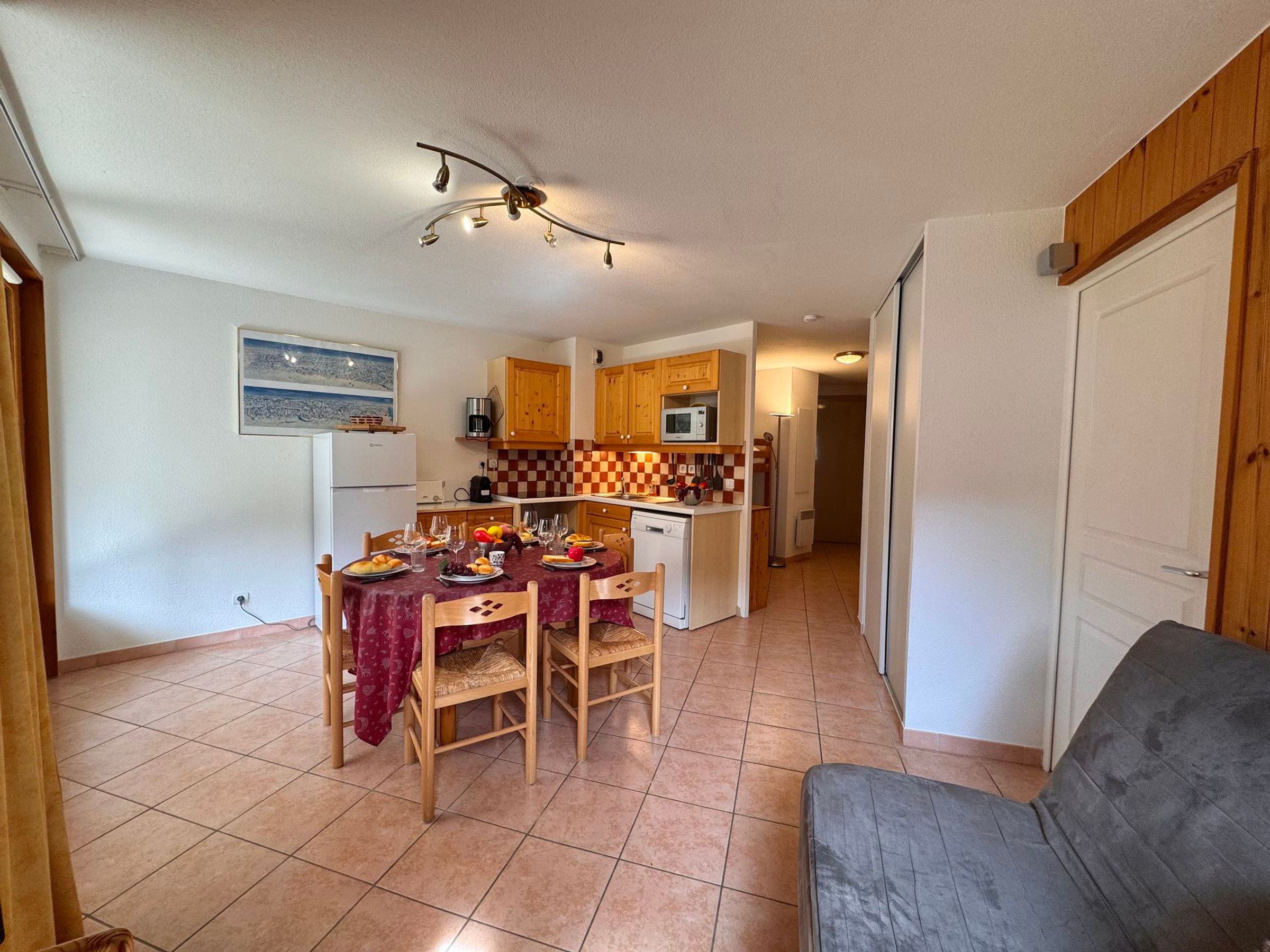 A compact kitchen with wooden cabinets, a dining table set for four, and a gray sofa in the living area.