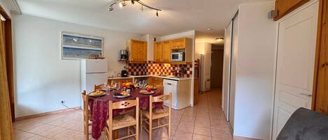 A compact kitchen with wooden cabinets, a dining table set for four, and a gray sofa in the living area.