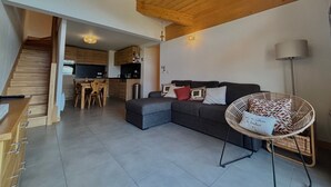 Un salon moderne avec un canapé gris, un fauteuil en osier et un escalier menant à la cuisine.