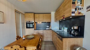 Une cuisine compacte avec des meubles en bois, un four encastré, une machine à café et une table à manger avec des chaises.
