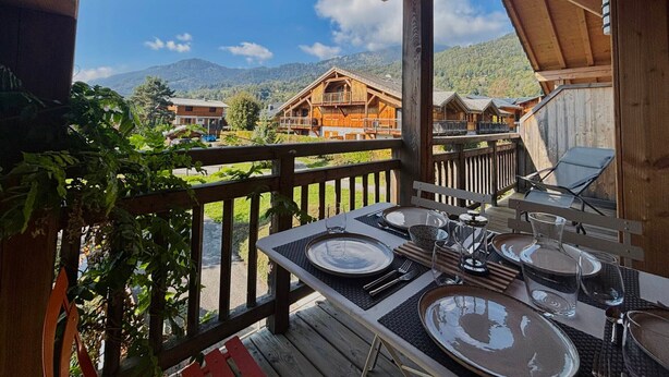 Une terrasse en bois avec une table dressée pour le repas, offrant une vue sur un paysage montagneux.