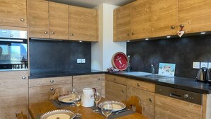 Une cuisine moderne avec des meubles en bois, un plan de travail noir et un coin repas aménagé pour quatre personnes.