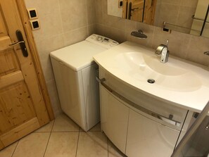 A compact laundry room with a washing machine, a sink, and a wooden door.