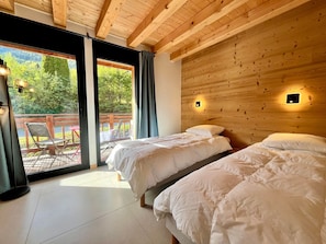 A room with two beds, a wooden ceiling, and a view of a deck with outdoor furniture.